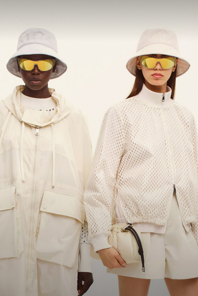 Two women wearing white jackets and mirrored sunglasses