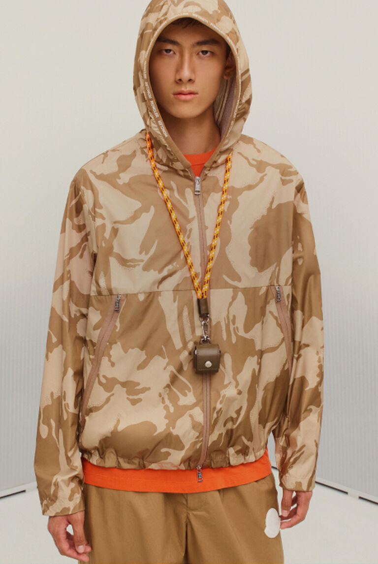 A man wearing a Moncler hooded jacket and beige trousers
